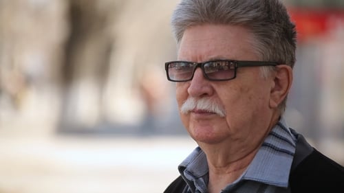A Wise Old Man with Mustache and Sunglasses Stands on a Street in Spring