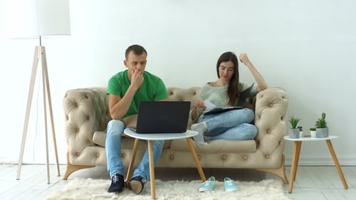 Couple Discussing Documents with Laptop on Sofa Indoors
