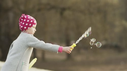 Child Blowing Bubbles Outside on Sunny Day