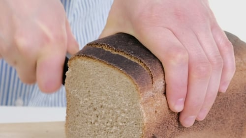 Slicing Dark Bread with Serrated Knife in Kitchen