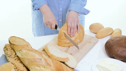 Woman Slices Bread on Cutting Board with Knife