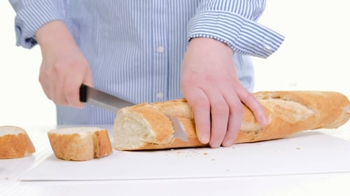 Person Slicing Baguette Bread on Cutting Board