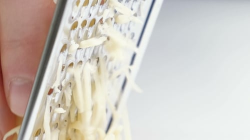 Gelber Käse mit einer Metallreibe von Hand reiben