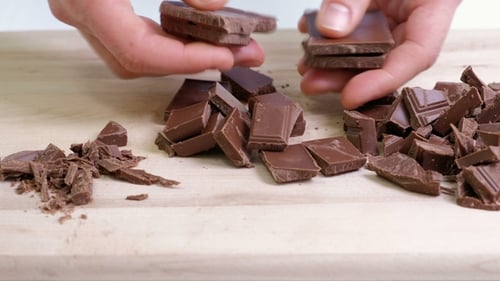 Cook Hands Cutting Chocolate Bar with a Kitchen Knife on Cutting Board.