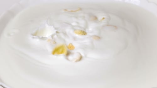 Corn Flakes Falling into Creamy Milk Bowl