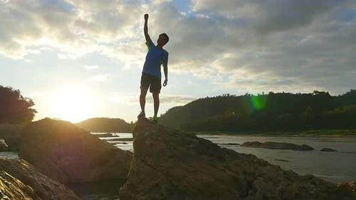 Triumphant Man Raising Fist on Rocky River Outcrop