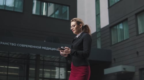 Businesswoman Walks with Phone and Coffee Outdoors