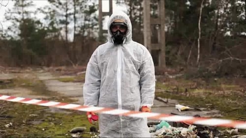 Man in Bio-hazard Suit and Gas Masks Stands Behind the Stripe on the Territory Full of Waste
