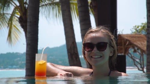 Young Woman Drinking Cocktail in Swimming Pool with Seaview