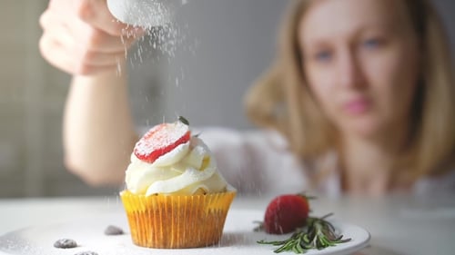 Woman Garnishing Cupcake with Powdered Sugar