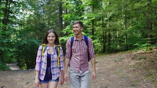 Young Couple of Tourists with Backpacks Walking in the Woods. Warm Summer Day