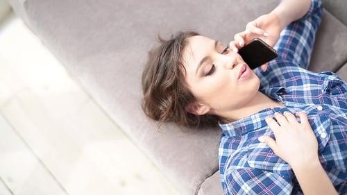 Happy Woman Talking on Cellphone Lying on Couch