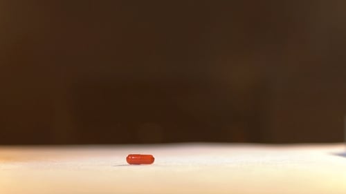 Hand Picking Up Red Capsule Pill Close-Up