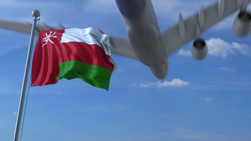 Commercial Airplane Flying Above Waving Flag of Oman