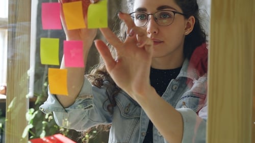 Young Attractive Woman Sticking Colored Memos on Glass Board in Modern Office