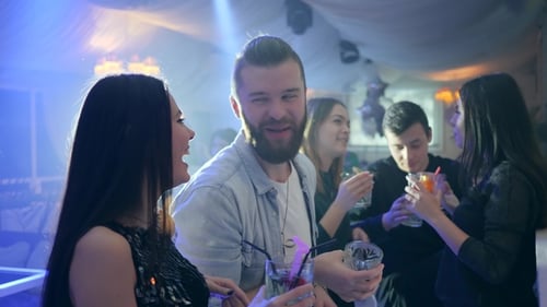 Guy and Cute Girl Hold Cocktails and Talks near Bar Counter Against the Background of People