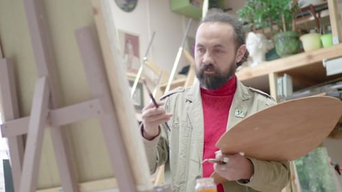 Man Artist in Apron Painting Picture on Canvas in Art Studio