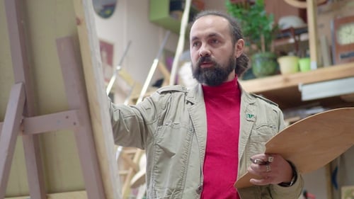 Man Artist in Apron Painting Picture on Canvas in Art Studio