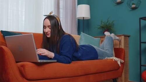 Young Woman Using Laptop Computer Sitting on Sofa at Home Working Online Shopping From Home Office