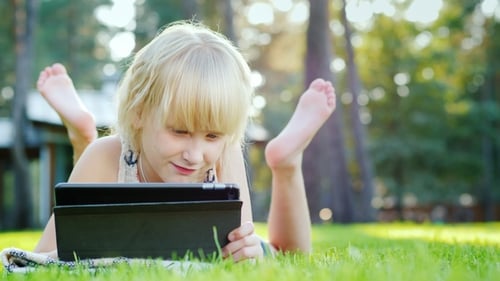 On the Green Lawn Near Her House Lies a Girl of 6 Years Old, Playing on a Tablet