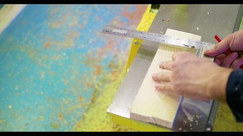 Ein Mann in einer Schreinerei markiert eine Tafel mit einem Bleistift.