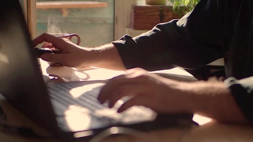 A Man Is Working on a Laptop. He Drinks Hot Tea. Focus on a Cup of Tea.