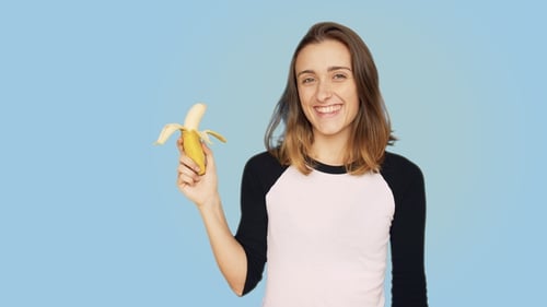 Smiling Woman Holding Peeled Banana on Blue Background