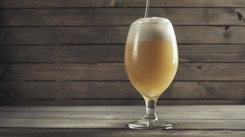 Beer Pouring into Glass on Rustic Wooden Background