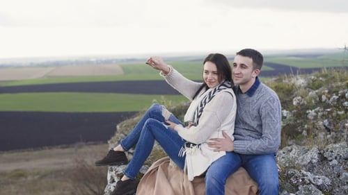 Lovely Couple Resting in Embraces on the Rock in Windy Day.