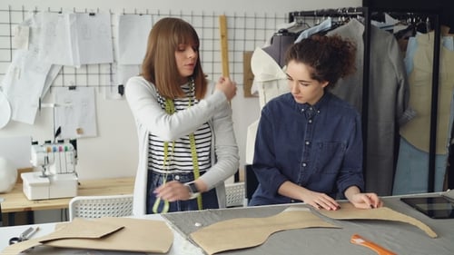 Experienced Tailor Is Teaching Young Woman To Sew Sleeves. She Is Talking, Gesturing, Showing