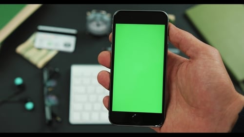 Man Holds Smartphone with Green Screen Over a Working Table