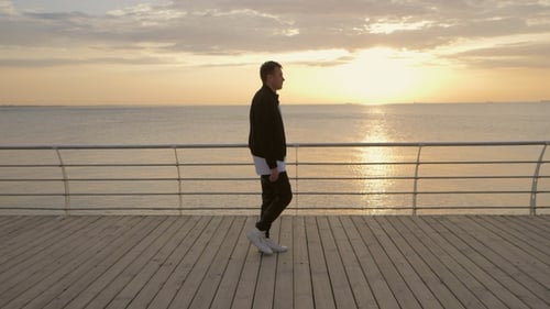 Silhouette of Young Trendy Modern Man Walking To Right Side Along Wooden Embankment Near Sea or