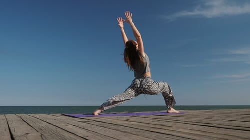 Junge fröhliche Frau macht Yoga Asana in der Natur am Holzstrand in der Nähe von Meer oder Meer. Mädchen in