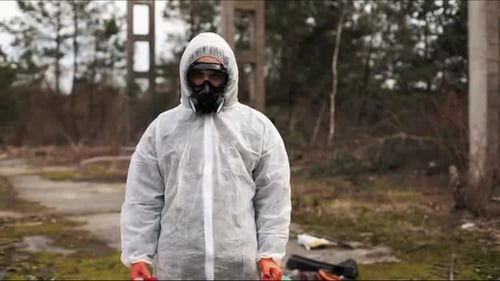 Mann im Biogefahrenanzug und Gasmasken steht hinter dem Streifen auf dem Gebiet voller Müll