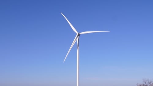 Große Windmühlenblätter drehen sich in der Luft vor blauem Himmel