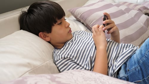 Boy Lies on Couch Using Cellphone Indoors