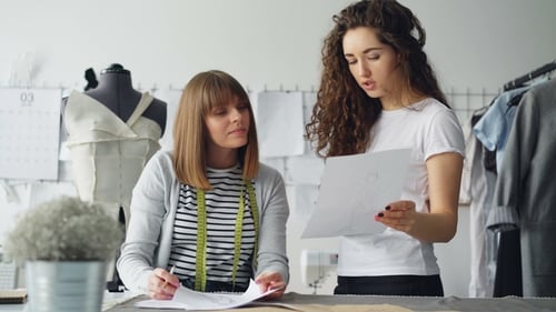 Professional Female Fashion Designers Are Looking at Sketch and Discussing Details