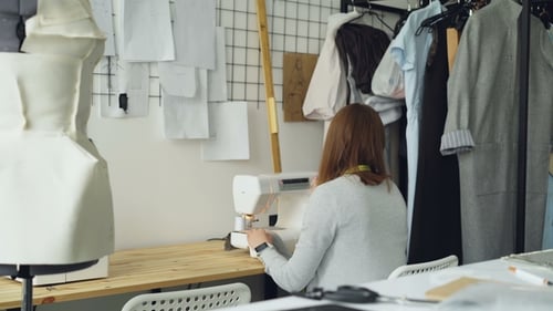 Young Woman Clothing Designer Working with Sewing Machine Sitting at Studio Desk