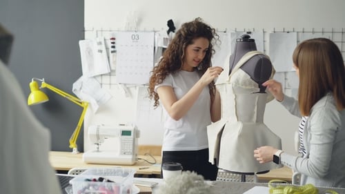 Kreative weibliche Bekleidungsdesigner heften beim Zuschneiden ausgeschnittene Stoffstücke an den Schnuller