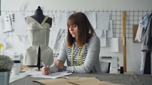 Clothing Designer in Small Start-up Business Is Drawing Sketches for Women's Clothes and Thinking