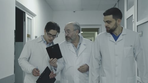 Three Male Doctors Discuss a Patient's Notes When Walk in Hospital Corridor.