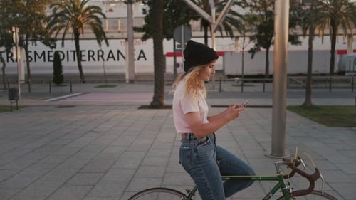 Woman with Phone on Bicycle in Urban Setting