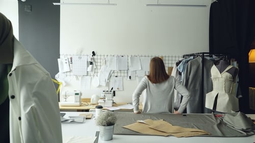 Young Designer Standing with Her Back To Camera and Looking at Drawings Hanging on Wall