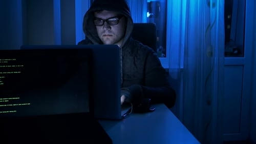 Footage of Young Male Hacker Wearing Eyeglasses and Hood Working at Laptop at Night