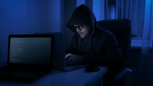 Funny Footage of Male Wearing Hood in Dark Room Pretends To Be Hacker. Man Working on Laptop a