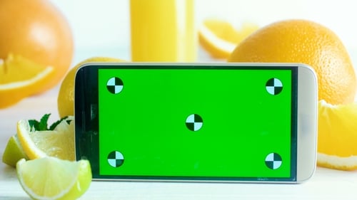 Footage of Mobile Phone with Chroma Key Green Screen Standing on Table Next To Glass of Juice n