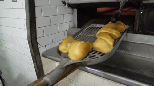 Eine Bäckerin holt heiße Brötchen aus dem Ofen