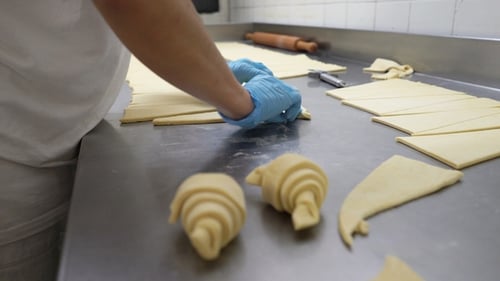 Baker Rolling Dough Into Croissants on Table