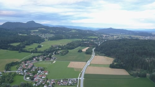 Aerial Footage of a Village and a Road between Green Fields and Forests on Sunset