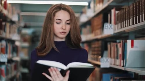 Thoughtful Young Female Student Reads a Book Standing in the Library